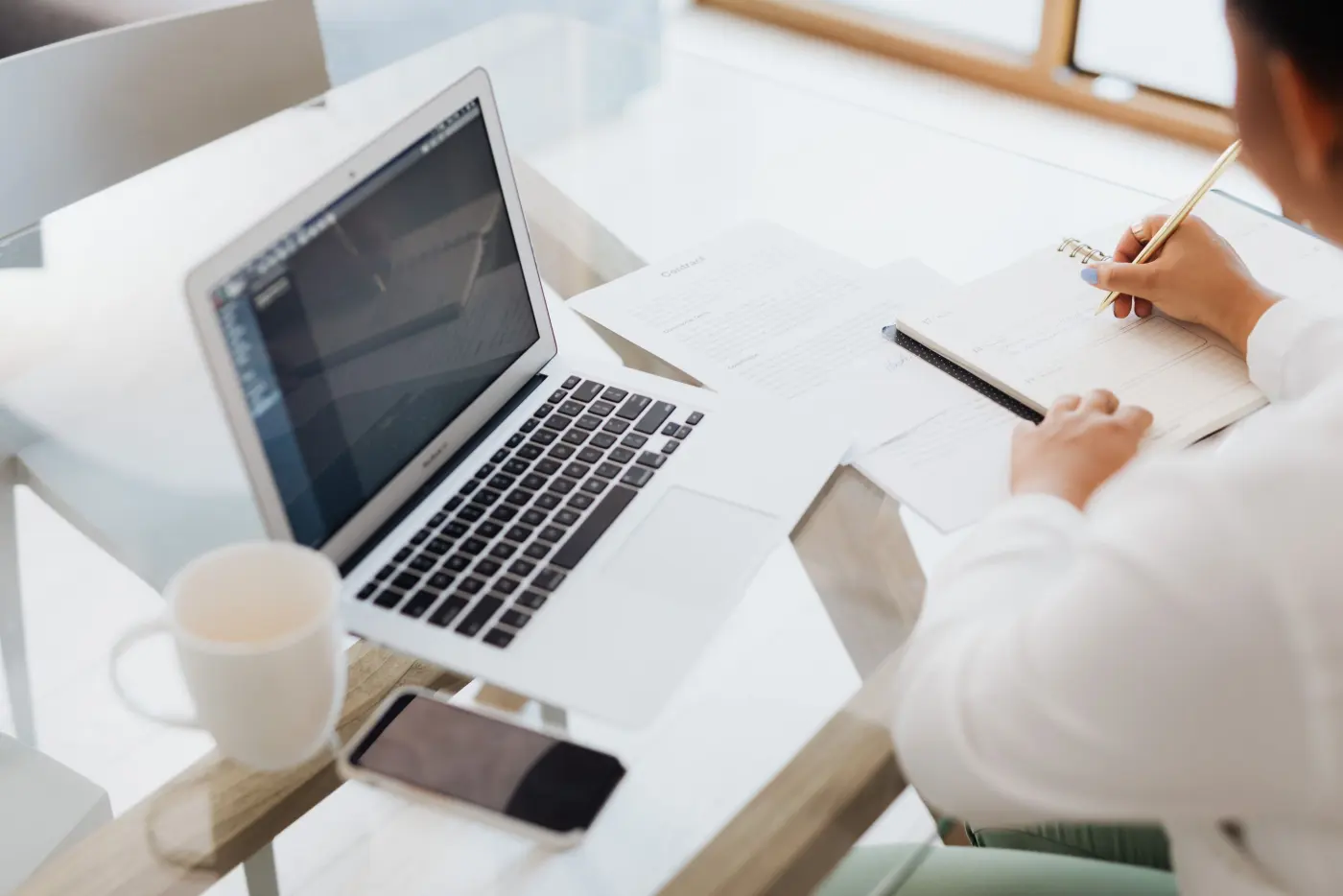 A laptop, notebook and coffee on a glass table