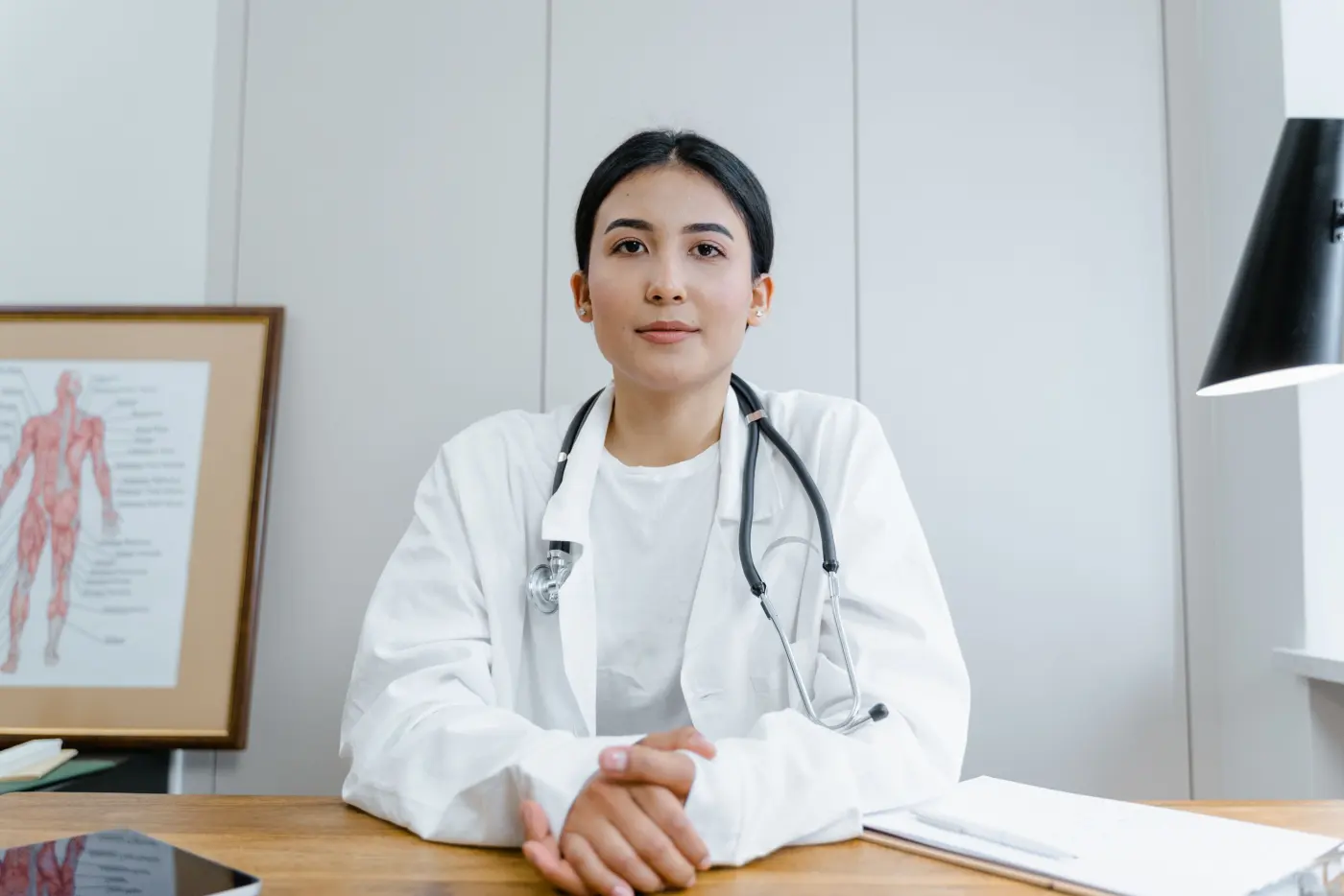 A doctor in a white coat with a stethoscope, seated at a clinic desk