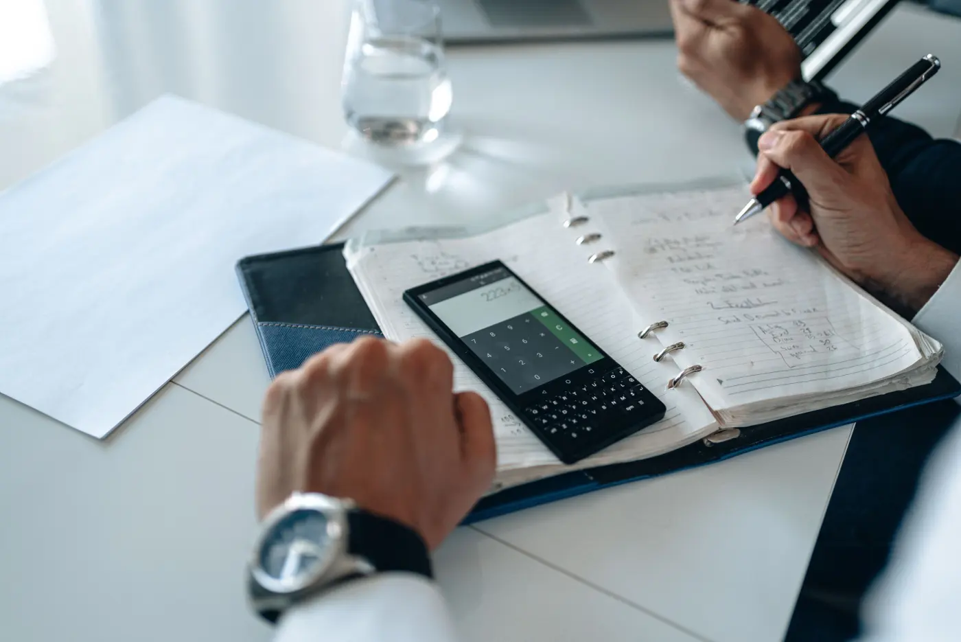 Hands with a calculator and a notebook open on a white desk