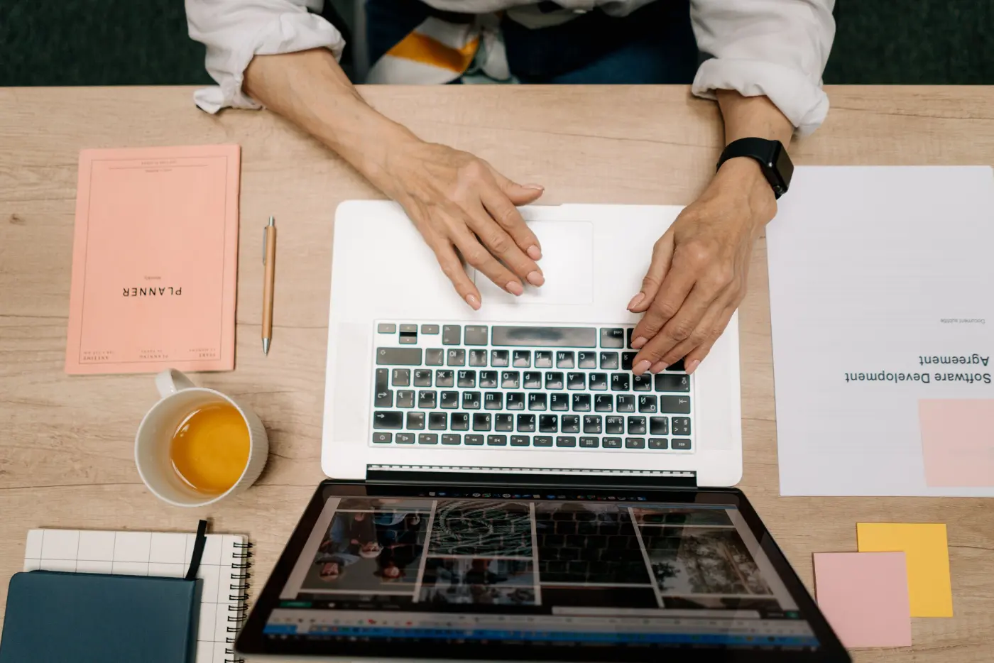 A laptop, a paper planner and a cup of tea on a wooden desk, seen from above